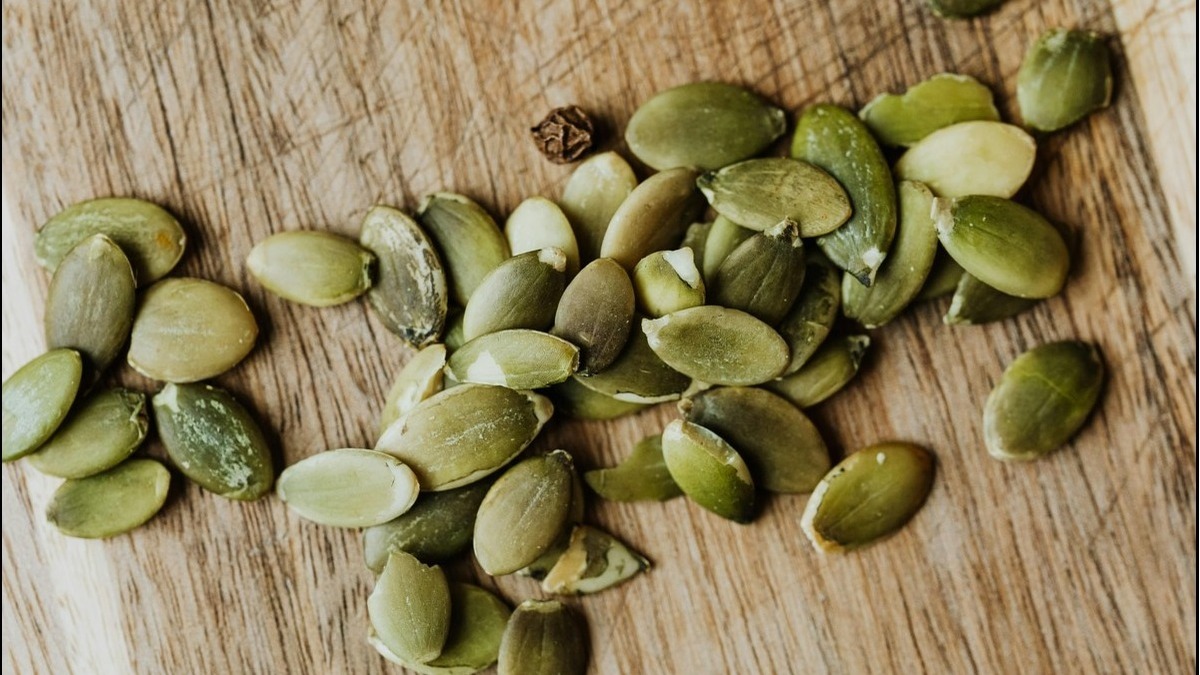 Handful of pumpkin seeds (pepitas) on a wooden surface.