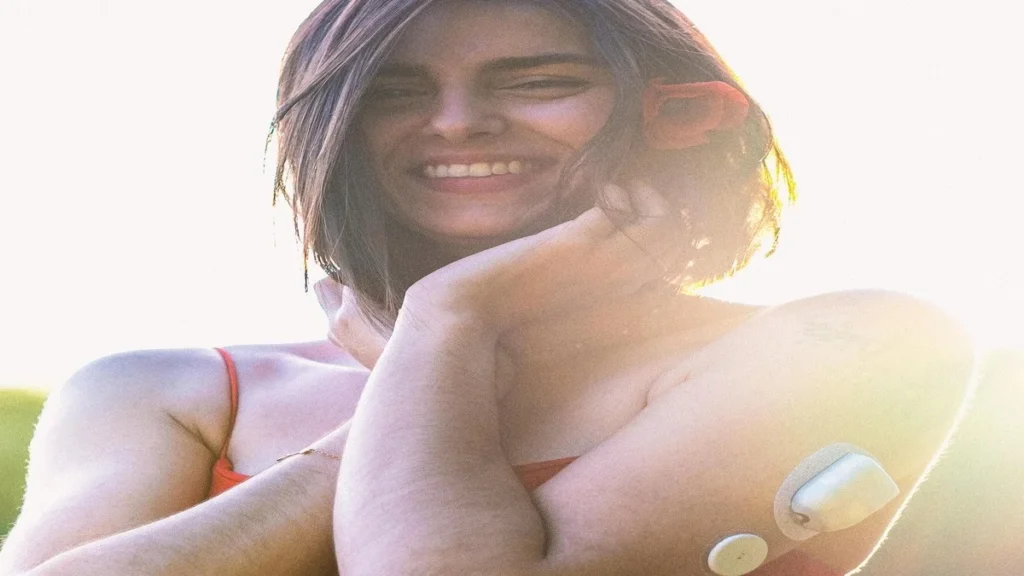 Continuous glucose monitor sensor on a person’s arm with smartphone displaying glucose graph