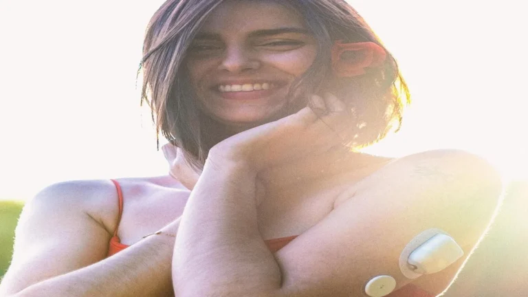 Continuous glucose monitor sensor on a person’s arm with smartphone displaying glucose graph