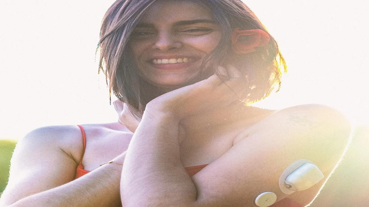 Continuous glucose monitor sensor on a person’s arm with smartphone displaying glucose graph