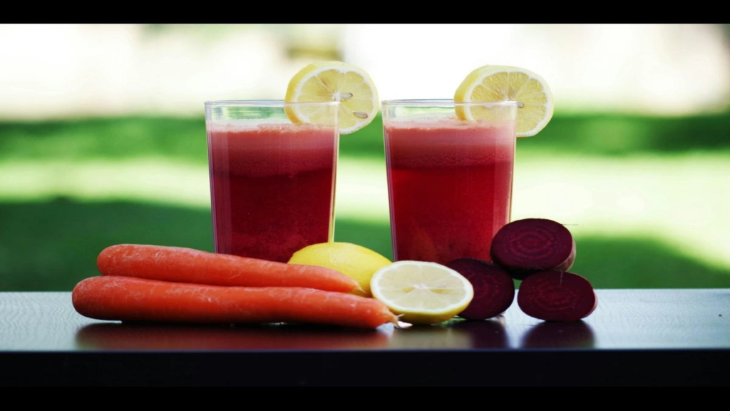Glass of deep‑red crimson elixir juice with fruits in background.