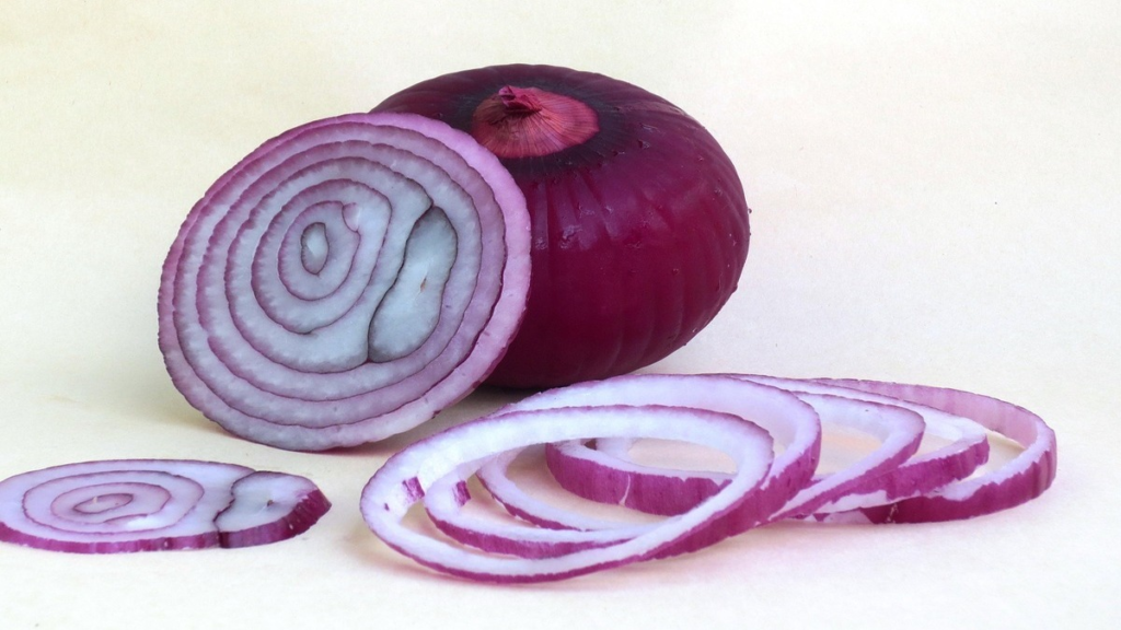 Whole and sliced onions on a wooden board.