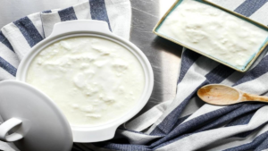 Bowl of plain yogurt next to a glass of milk.