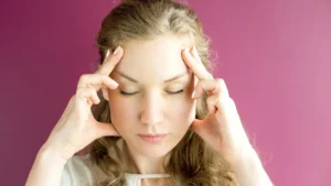 Woman experiencing a severe migraine attack while holding her head in a dark room with low lighting.