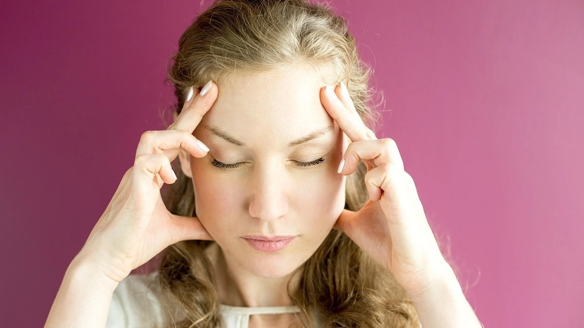 Woman experiencing a severe migraine attack while holding her head in a dark room with low lighting.