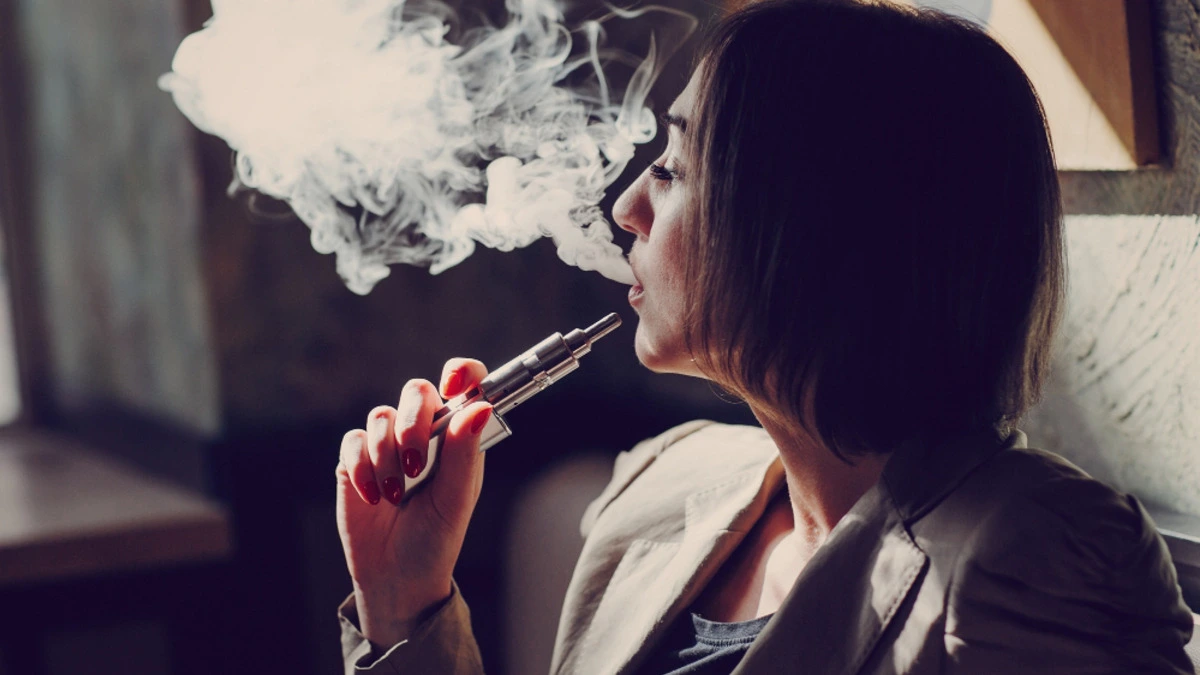 Person using an e-cigarette with DNA strand illustration representing vaping and cancer risk
